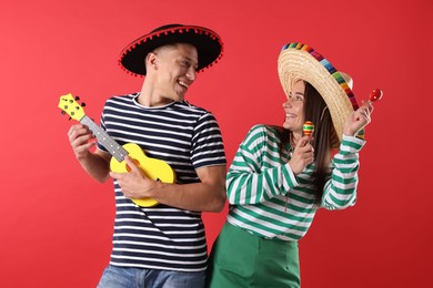 Photo of Happy couple in sombrero and Flamenco hats playing musical instruments on red background