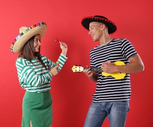 Photo of Happy couple in sombrero and Flamenco hats playing musical instruments on red background