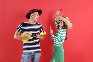 Photo of Happy couple in sombrero and Flamenco hats playing musical instruments on red background