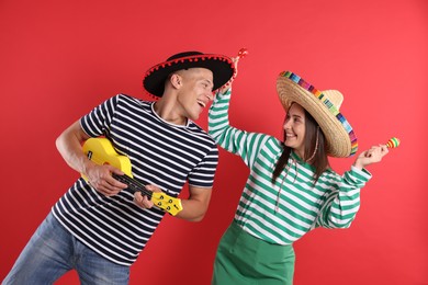 Photo of Happy couple in sombrero and Flamenco hats playing musical instruments on red background