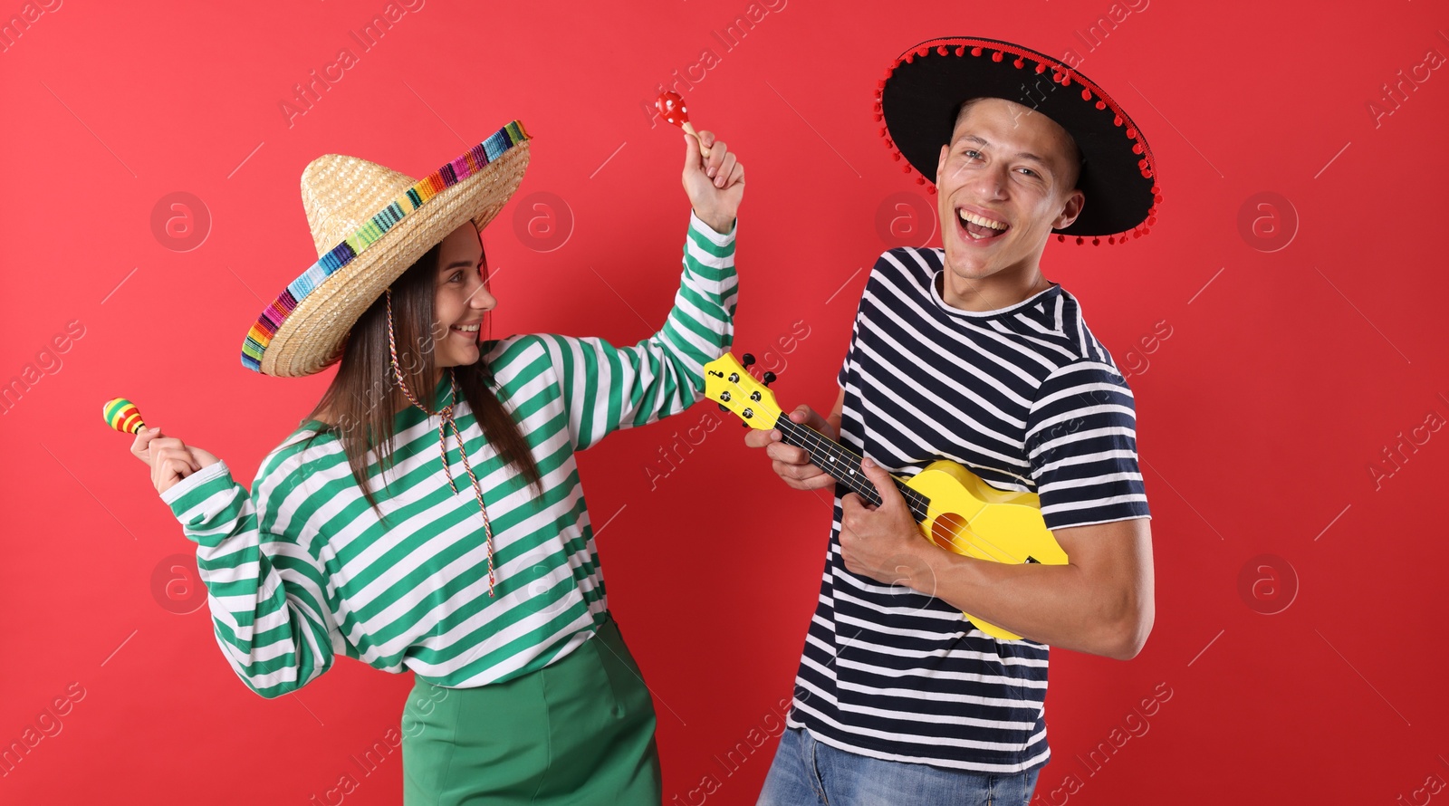 Photo of Happy couple in sombrero and Flamenco hats playing musical instruments on red background