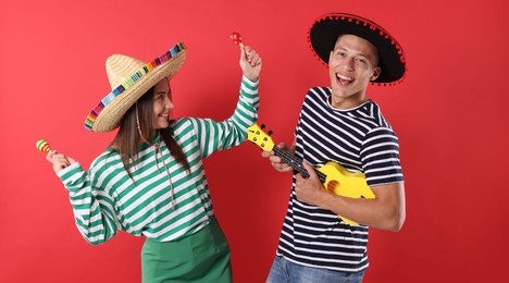 Photo of Happy couple in sombrero and Flamenco hats playing musical instruments on red background