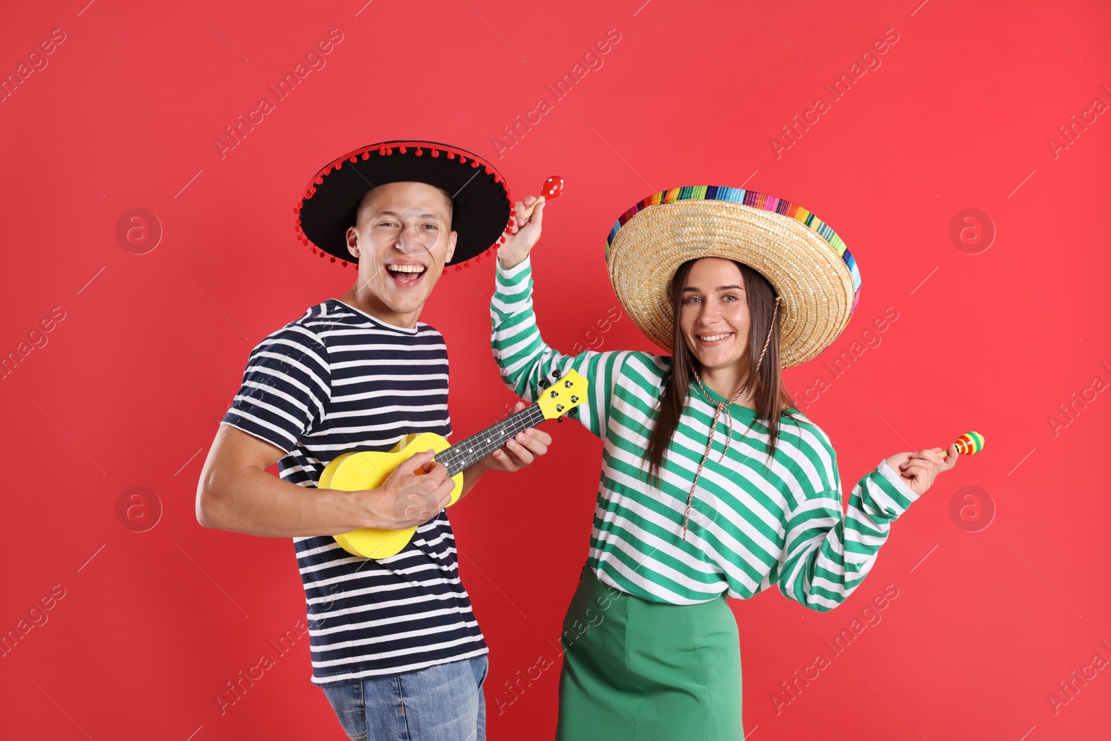 Photo of Happy couple in sombrero and Flamenco hats playing musical instruments on red background