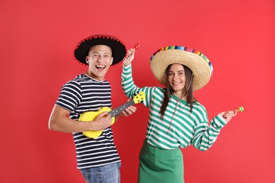 Photo of Happy couple in sombrero and Flamenco hats playing musical instruments on red background