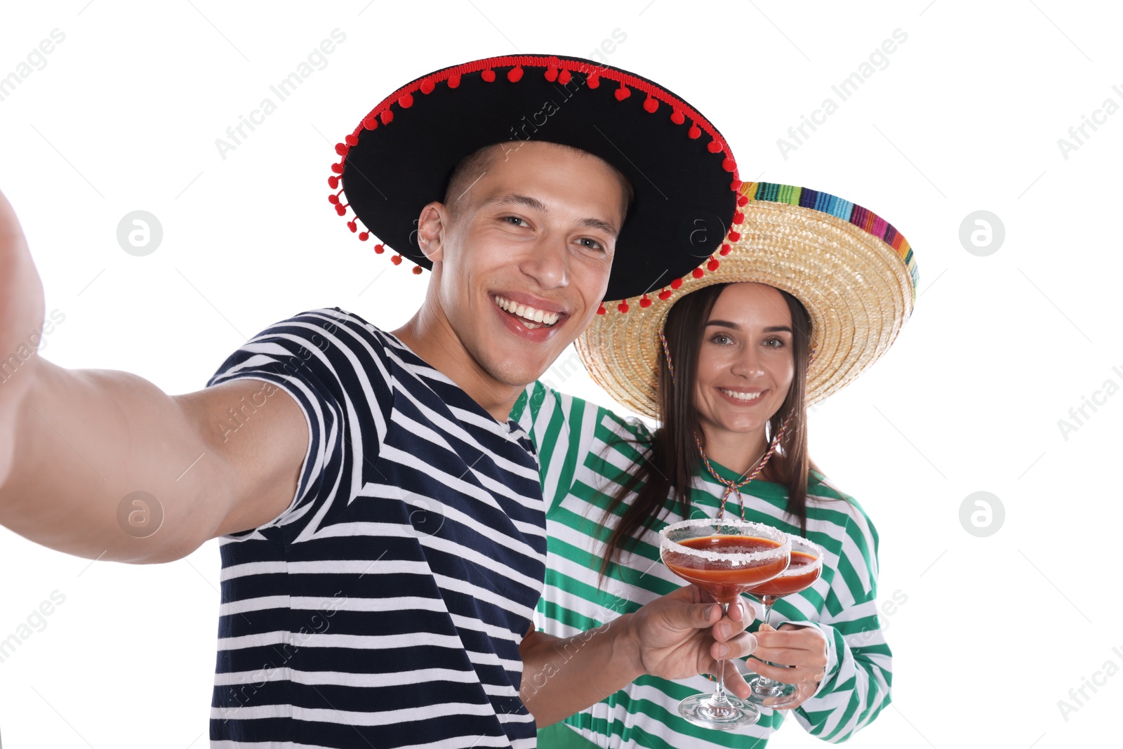 Photo of Happy couple in sombrero and Flamenco hats with cocktails taking selfie on white background