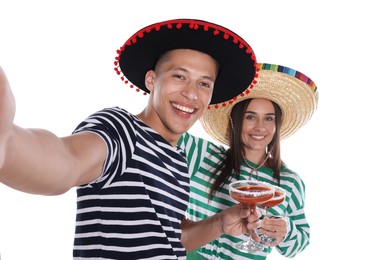 Photo of Happy couple in sombrero and Flamenco hats with cocktails taking selfie on white background