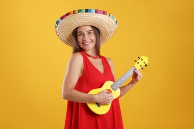 Photo of Happy woman in sombrero hat playing ukulele on yellow background