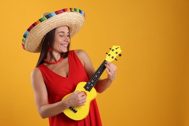 Photo of Happy woman in sombrero hat playing ukulele on yellow background. Space for text