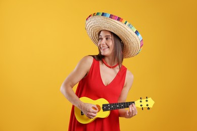 Photo of Happy woman in sombrero hat playing ukulele on yellow background