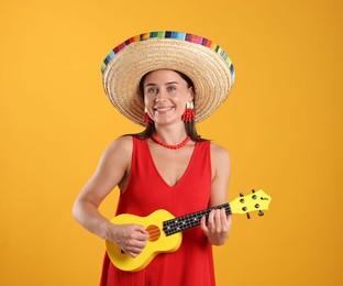 Photo of Happy woman in sombrero hat playing ukulele on yellow background
