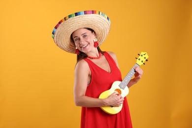 Photo of Happy woman in sombrero hat playing ukulele on yellow background