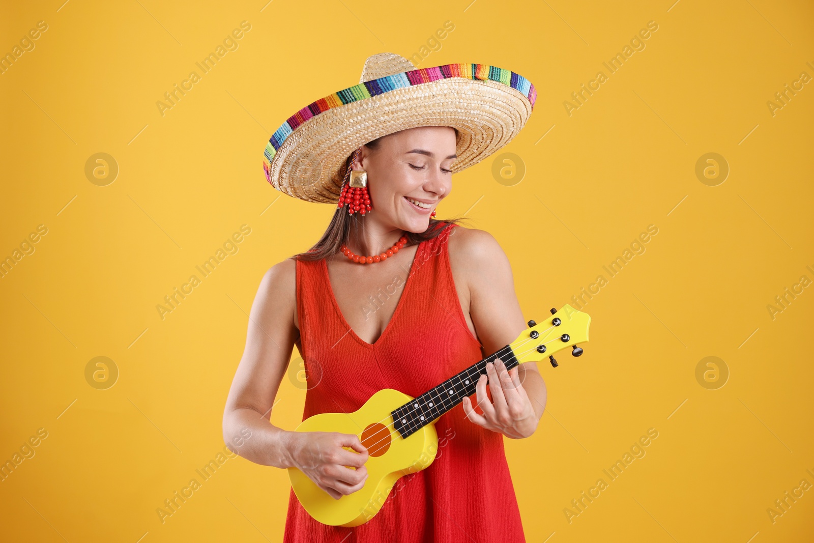 Photo of Happy woman in sombrero hat playing ukulele on yellow background