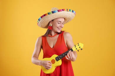 Photo of Happy woman in sombrero hat playing ukulele on yellow background