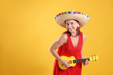 Photo of Happy woman in sombrero hat playing ukulele on yellow background. Space for text