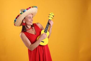 Photo of Happy woman in sombrero hat playing ukulele on yellow background. Space for text