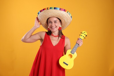 Photo of Happy woman in sombrero hat playing ukulele on yellow background