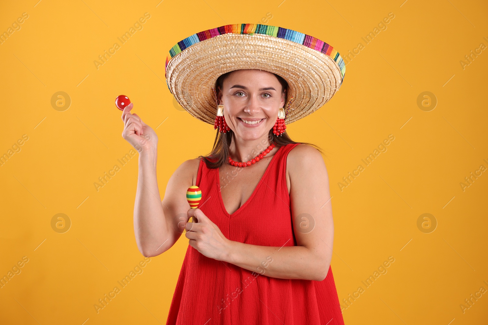 Happy woman in sombrero hat playing maracas on yellow background Photo of Happy woman in sombrero hat playing maracas on yellow background