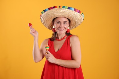 Photo of Happy woman in sombrero hat playing maracas on yellow background