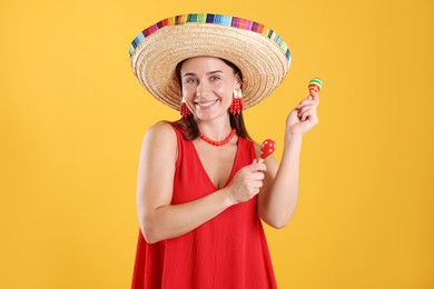 Photo of Happy woman in sombrero hat playing maracas on yellow background