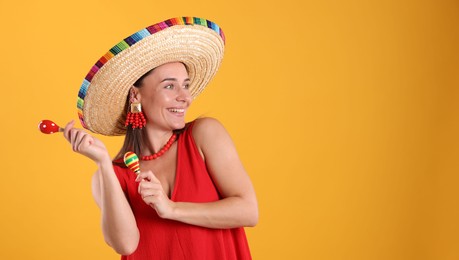 Photo of Happy woman in sombrero hat playing maracas on yellow background. Space for text