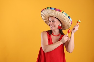 Photo of Happy woman in sombrero hat playing maracas on yellow background. Space for text