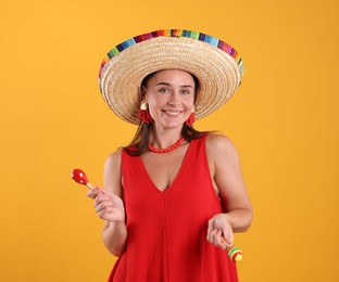 Photo of Happy woman in sombrero hat playing maracas on yellow background