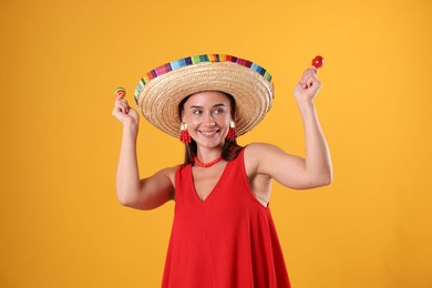 Photo of Happy woman in sombrero hat playing maracas on yellow background