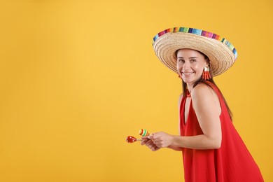 Photo of Happy woman in sombrero hat playing maracas on yellow background. Space for text