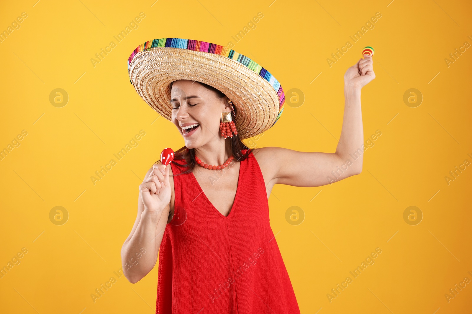 Happy woman in sombrero hat playing maracas and singing on yellow background Photo of Happy woman in sombrero hat playing maracas and singing on yellow background