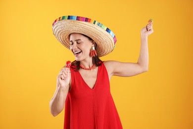 Photo of Happy woman in sombrero hat playing maracas and singing on yellow background