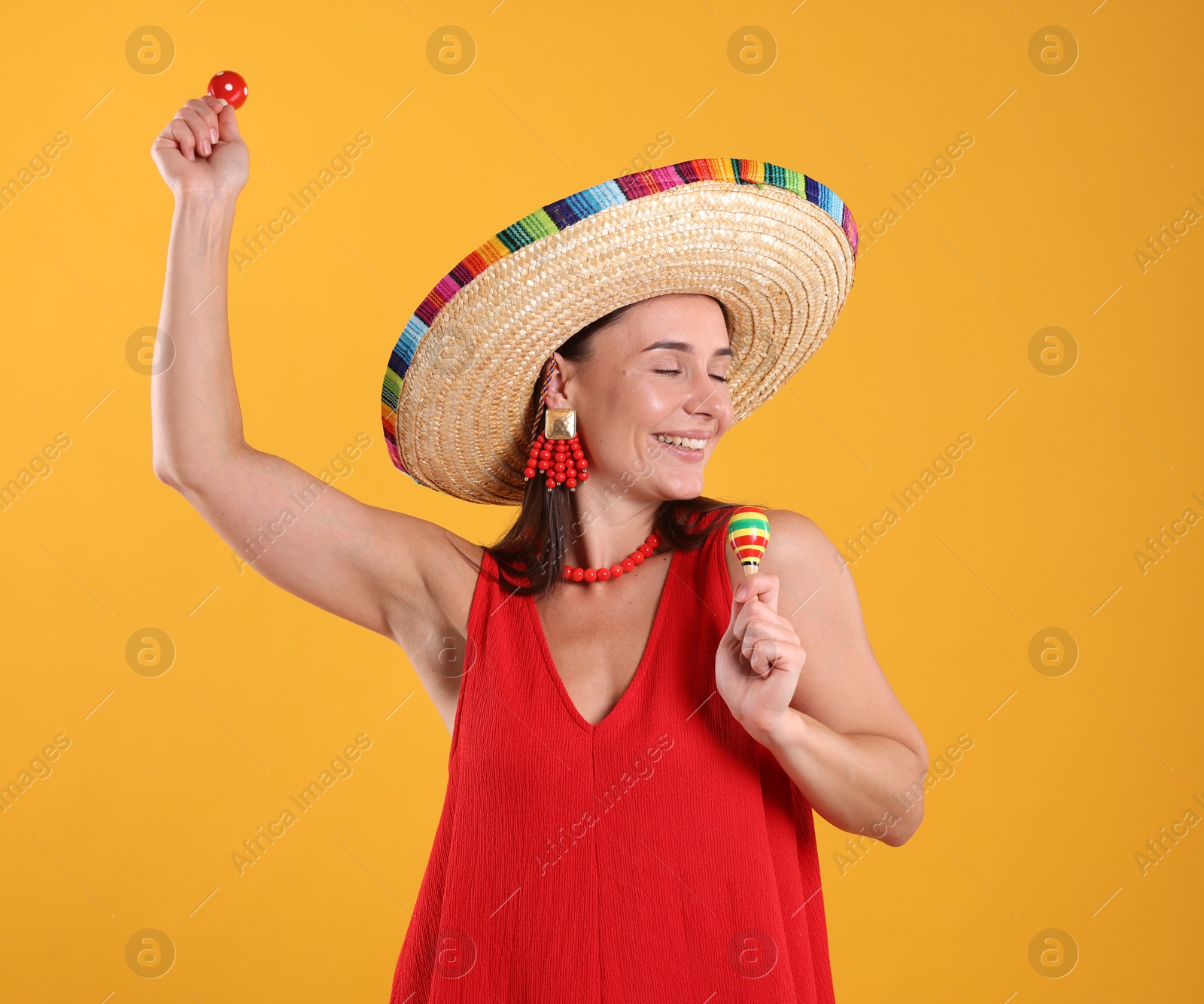 Happy woman in sombrero hat playing maracas on yellow background Photo of Happy woman in sombrero hat playing maracas on yellow background