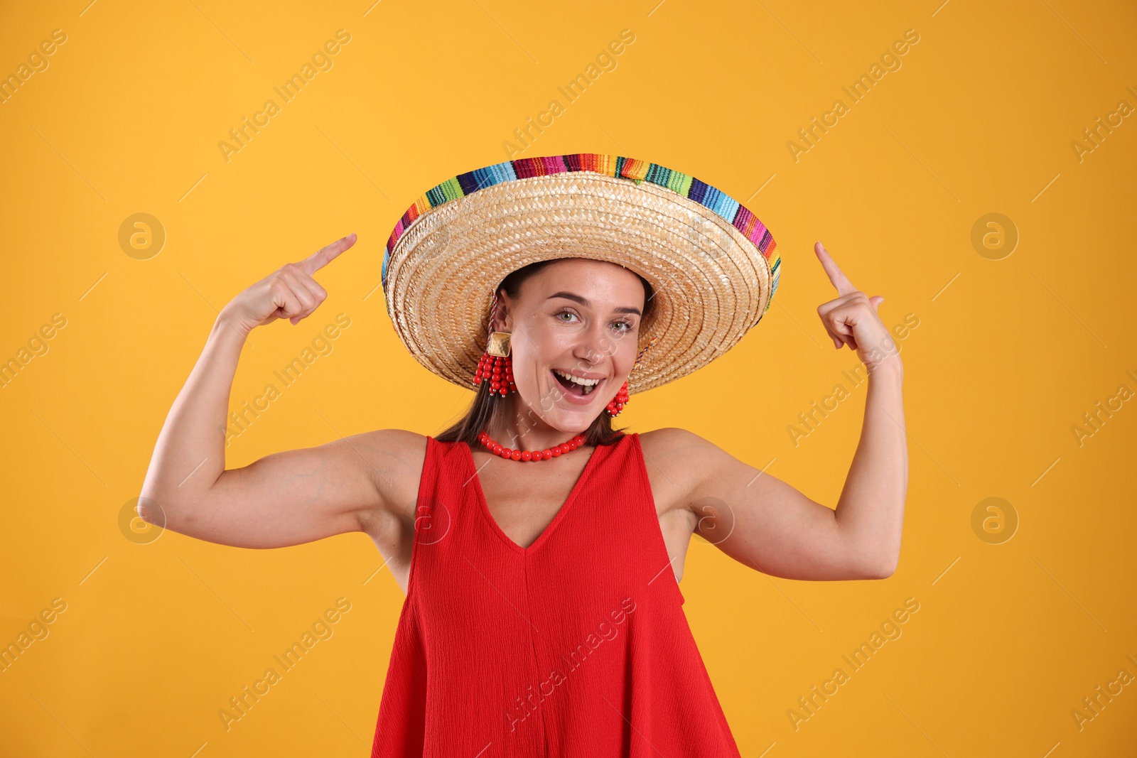 Happy woman pointing at her sombrero hat on yellow background Photo of Happy woman pointing at her sombrero hat on yellow background
