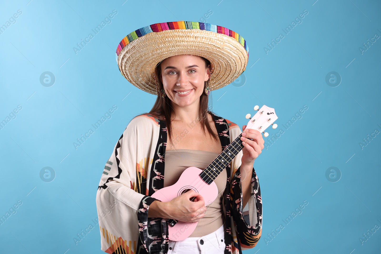 Happy woman in sombrero hat playing ukulele on light blue background Photo of Happy woman in sombrero hat playing ukulele on light blue background