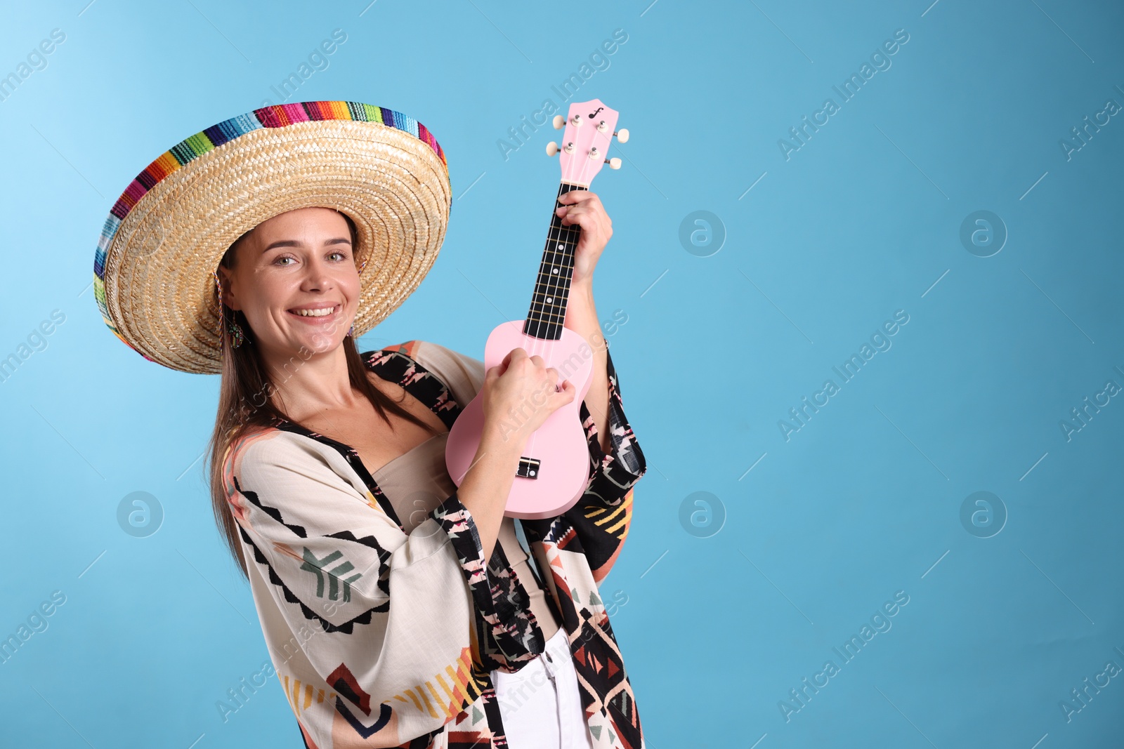 Happy woman in sombrero hat playing ukulele on light blue background. Space for text Photo of Happy woman in sombrero hat playing ukulele on light blue background. Space for text