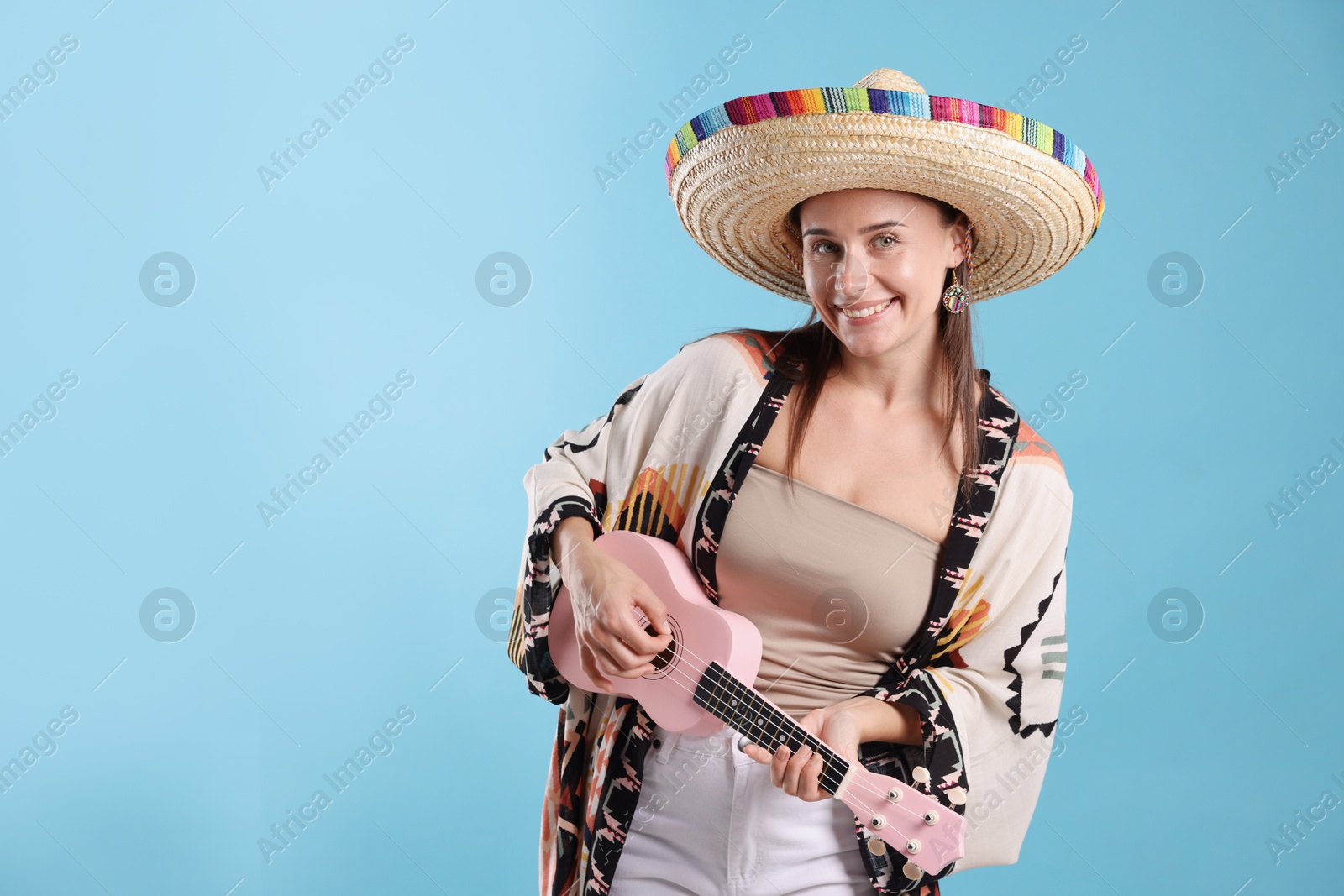 Happy woman in sombrero hat playing ukulele on light blue background. Space for text Photo of Happy woman in sombrero hat playing ukulele on light blue background. Space for text