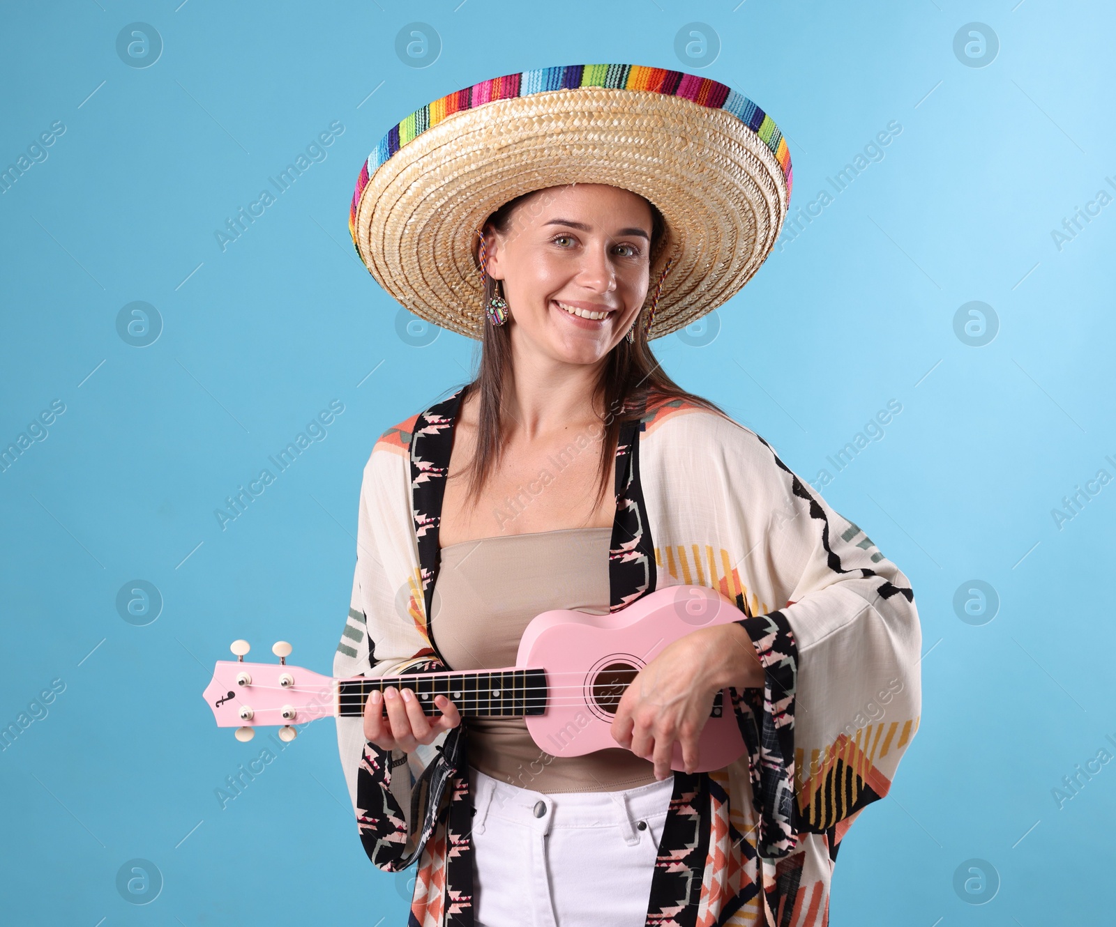 Happy woman in sombrero hat playing ukulele on light blue background Photo of Happy woman in sombrero hat playing ukulele on light blue background
