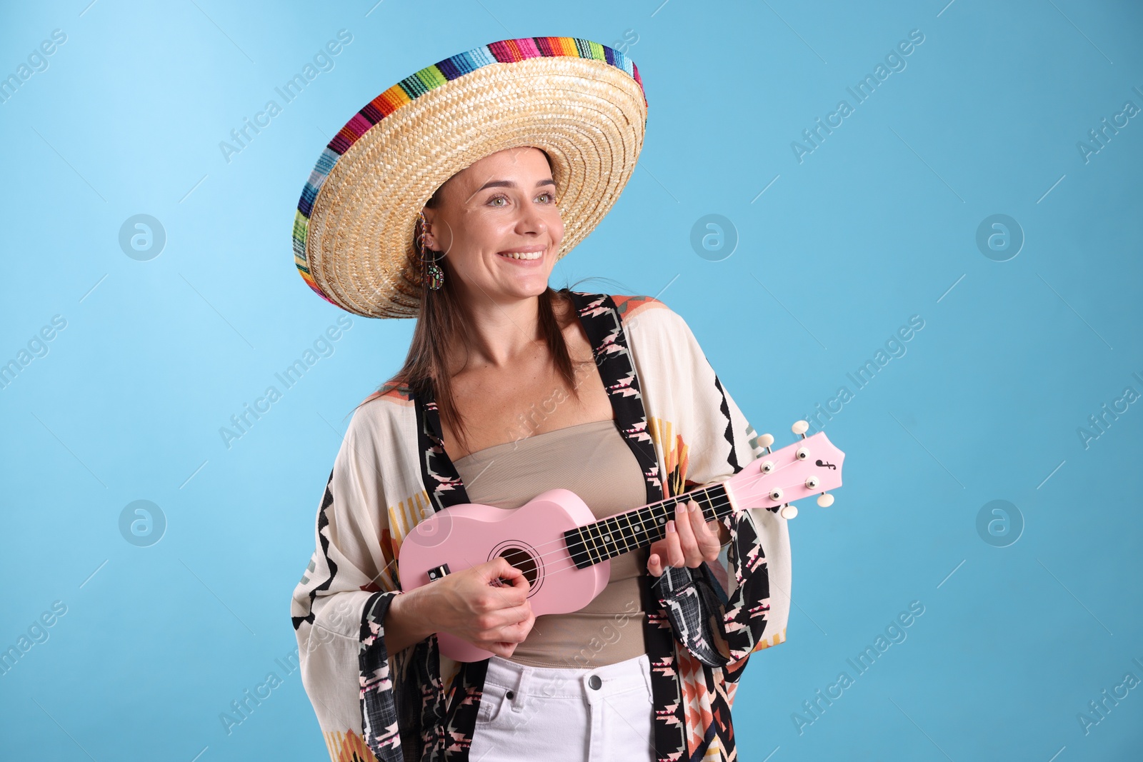 Happy woman in sombrero hat playing ukulele on light blue background Photo of Happy woman in sombrero hat playing ukulele on light blue background