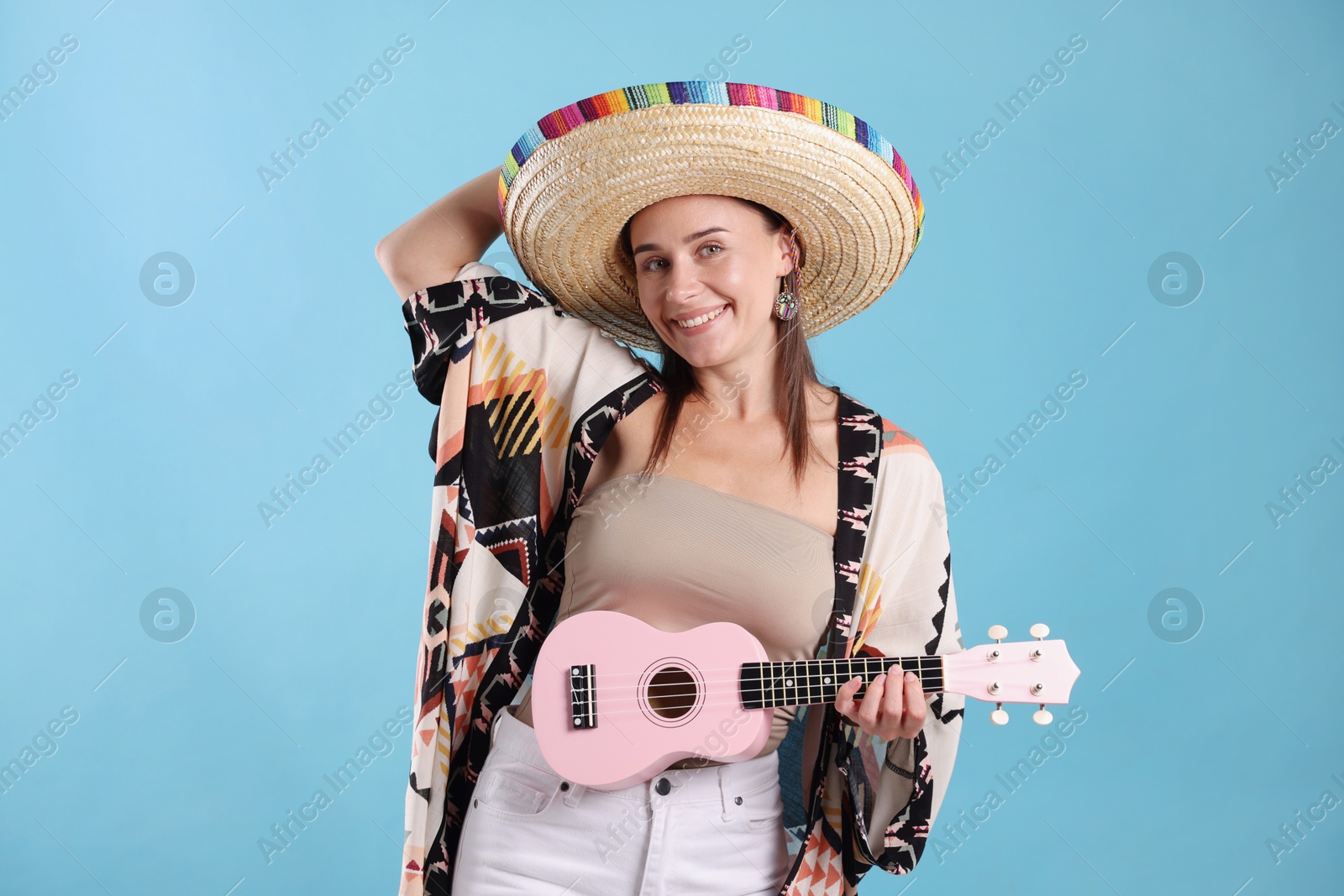 Happy woman in sombrero hat playing ukulele on light blue background Photo of Happy woman in sombrero hat playing ukulele on light blue background