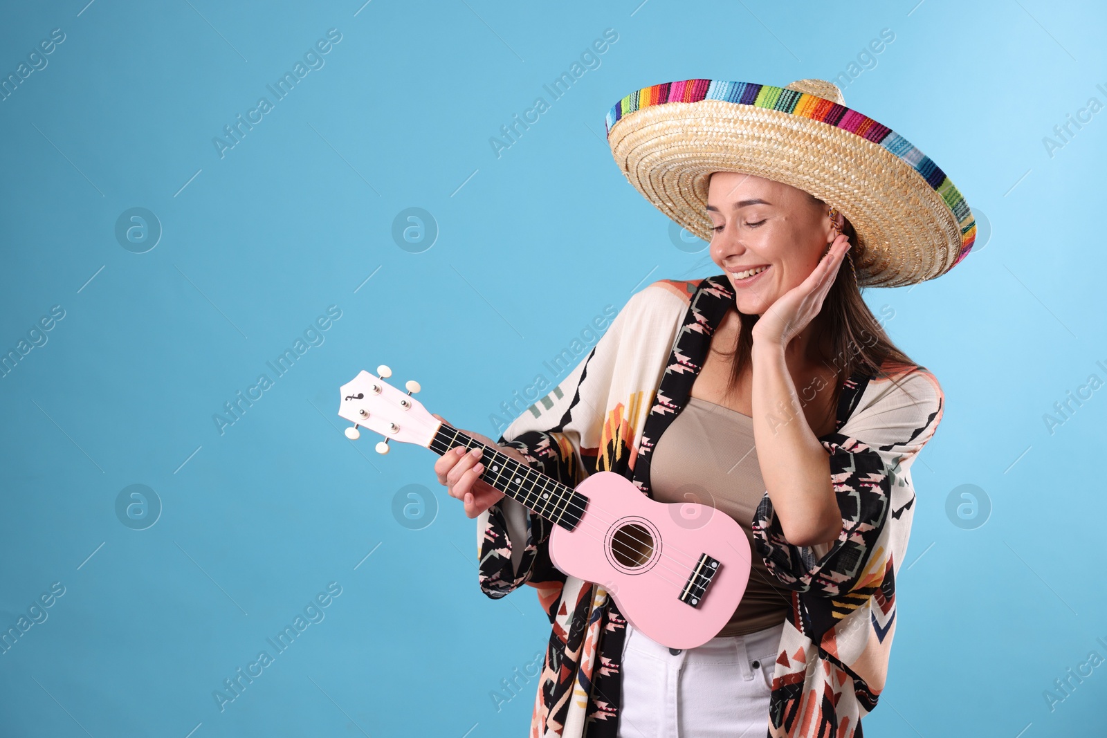 Happy woman in sombrero hat with ukulele on light blue background. Space for text Photo of Happy woman in sombrero hat with ukulele on light blue background. Space for text