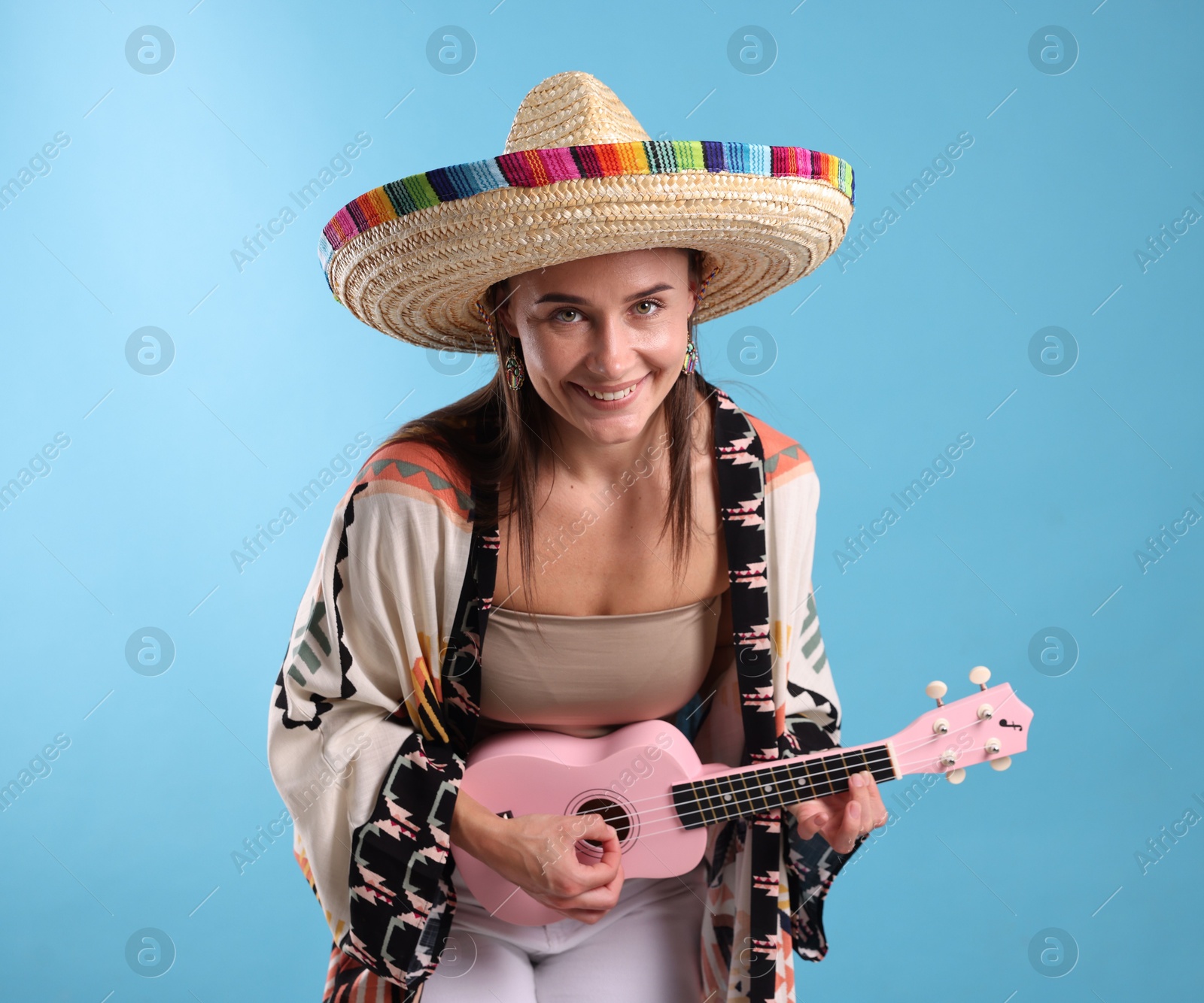 Happy woman in sombrero hat playing ukulele on light blue background Photo of Happy woman in sombrero hat playing ukulele on light blue background