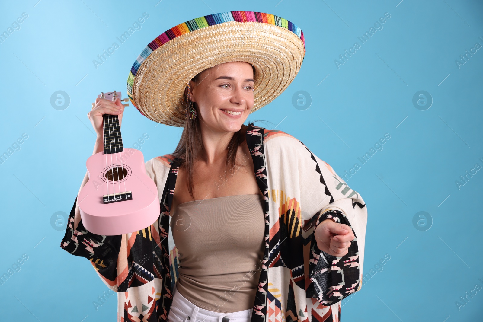 Happy woman in sombrero hat with ukulele on light blue background Photo of Happy woman in sombrero hat with ukulele on light blue background