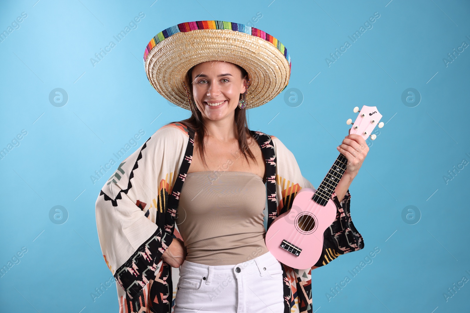 Happy woman in sombrero hat with ukulele on light blue background Photo of Happy woman in sombrero hat with ukulele on light blue background