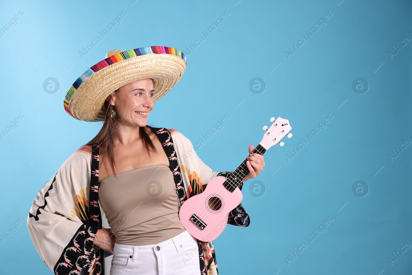Photo of Happy woman in sombrero hat with ukulele on light blue background. Space for text