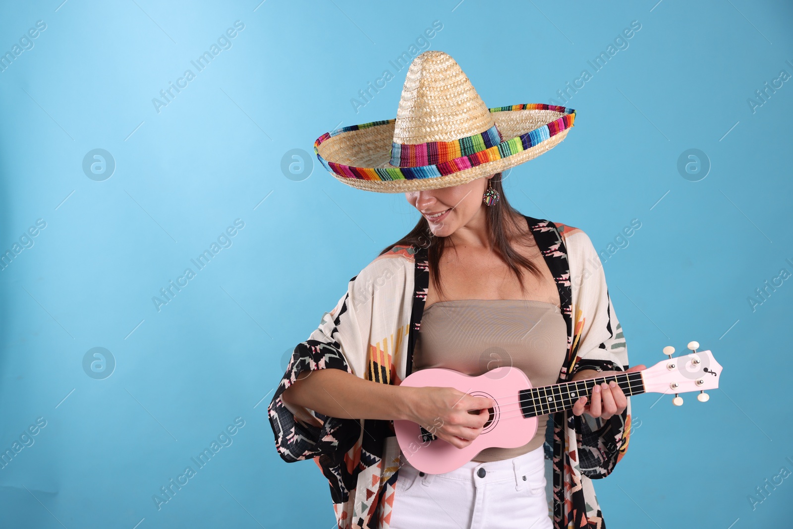 Happy woman in sombrero hat playing ukulele on light blue background. Space for text Photo of Happy woman in sombrero hat playing ukulele on light blue background. Space for text