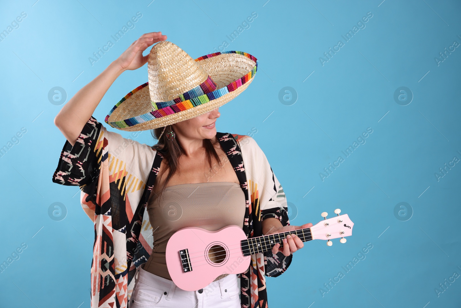 Photo of Happy woman in sombrero hat with ukulele on light blue background. Space for text
