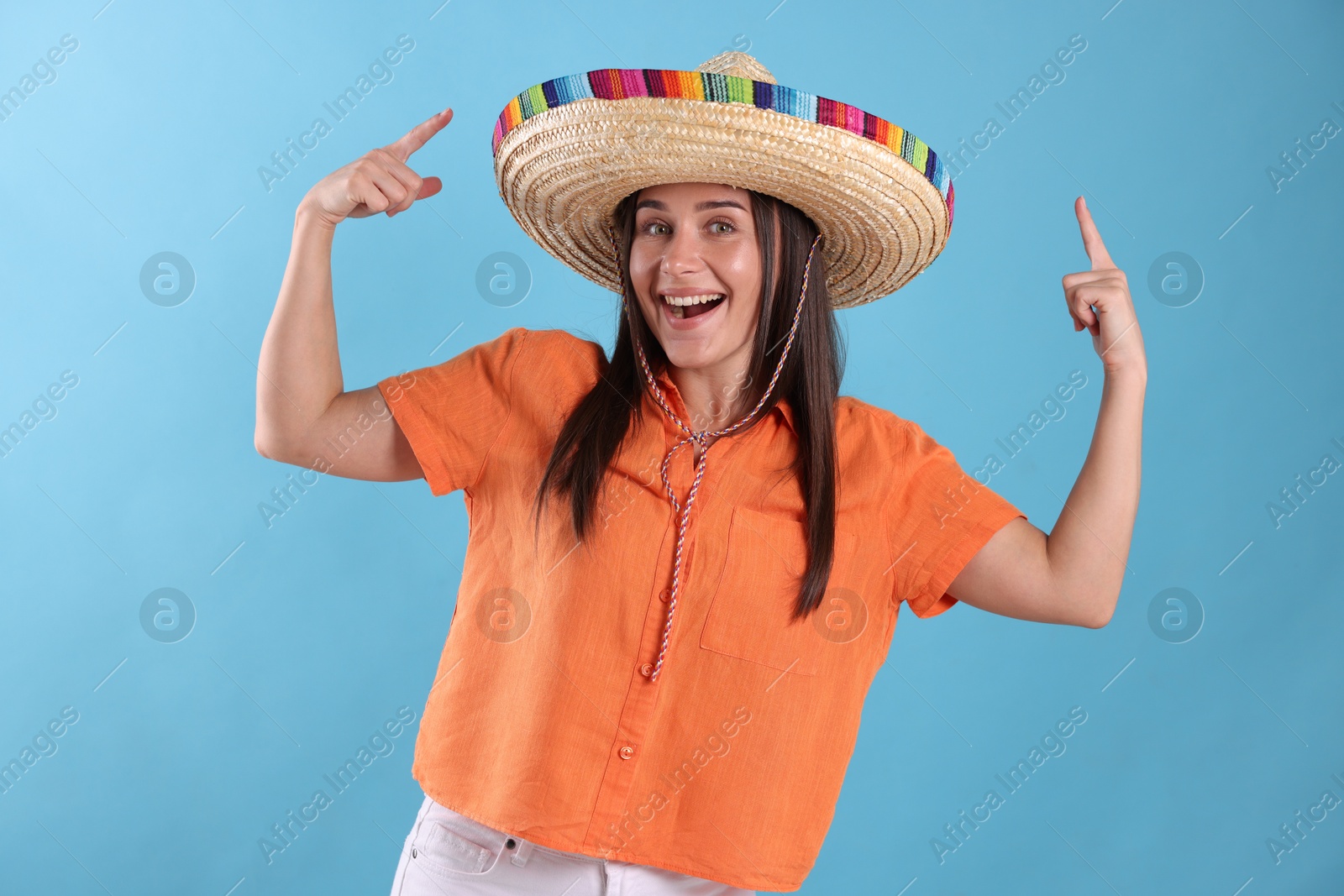 Happy woman pointing at her sombrero hat on light blue background Photo of Happy woman pointing at her sombrero hat on light blue background