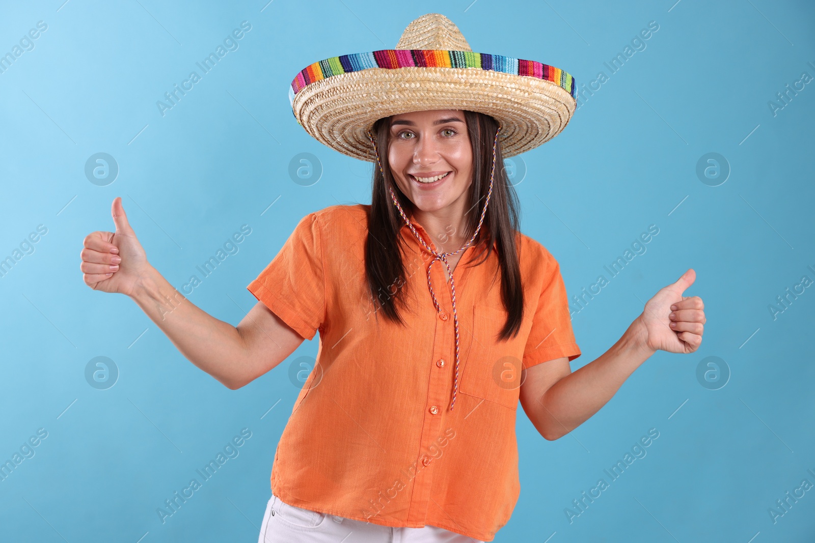 Happy woman in sombrero hat showing thumbs up on light blue background Photo of Happy woman in sombrero hat showing thumbs up on light blue background
