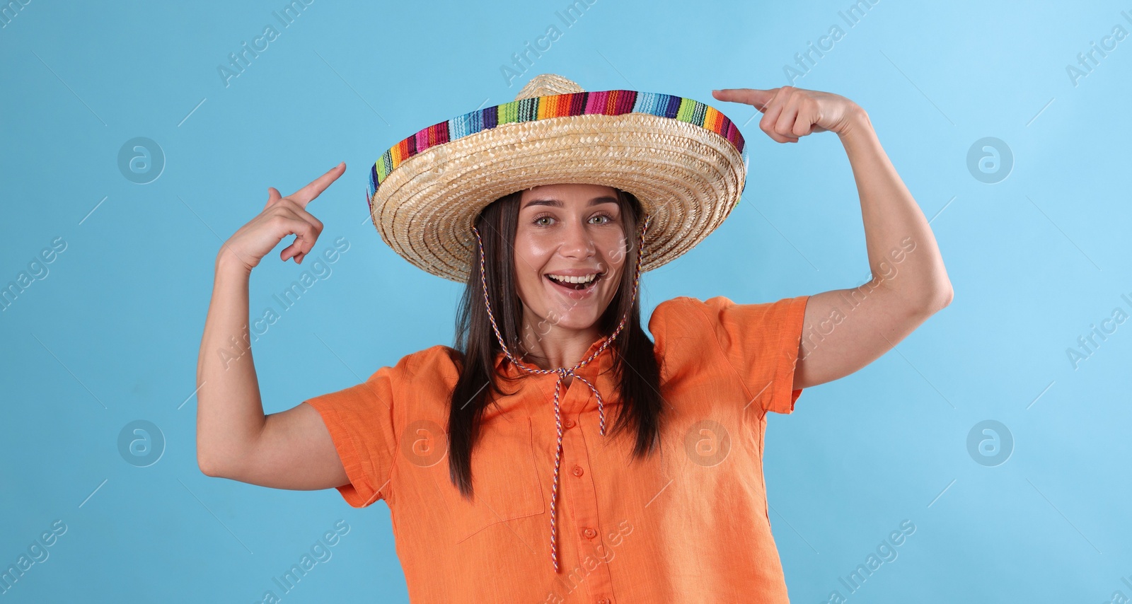 Happy woman pointing at her sombrero hat on light blue background Photo of Happy woman pointing at her sombrero hat on light blue background