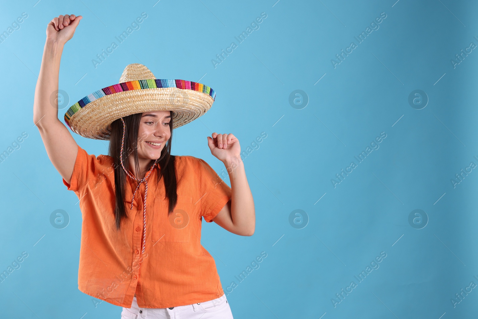 Happy woman in sombrero hat dancing on light blue background. Space for text Photo of Happy woman in sombrero hat dancing on light blue background. Space for text