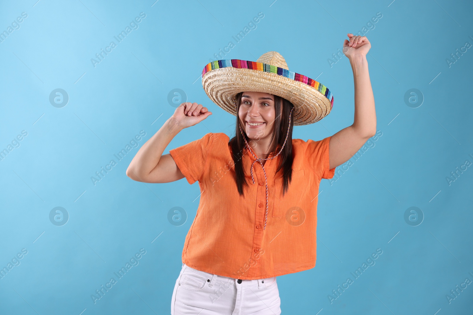 Happy woman in sombrero hat dancing on light blue background Photo of Happy woman in sombrero hat dancing on light blue background
